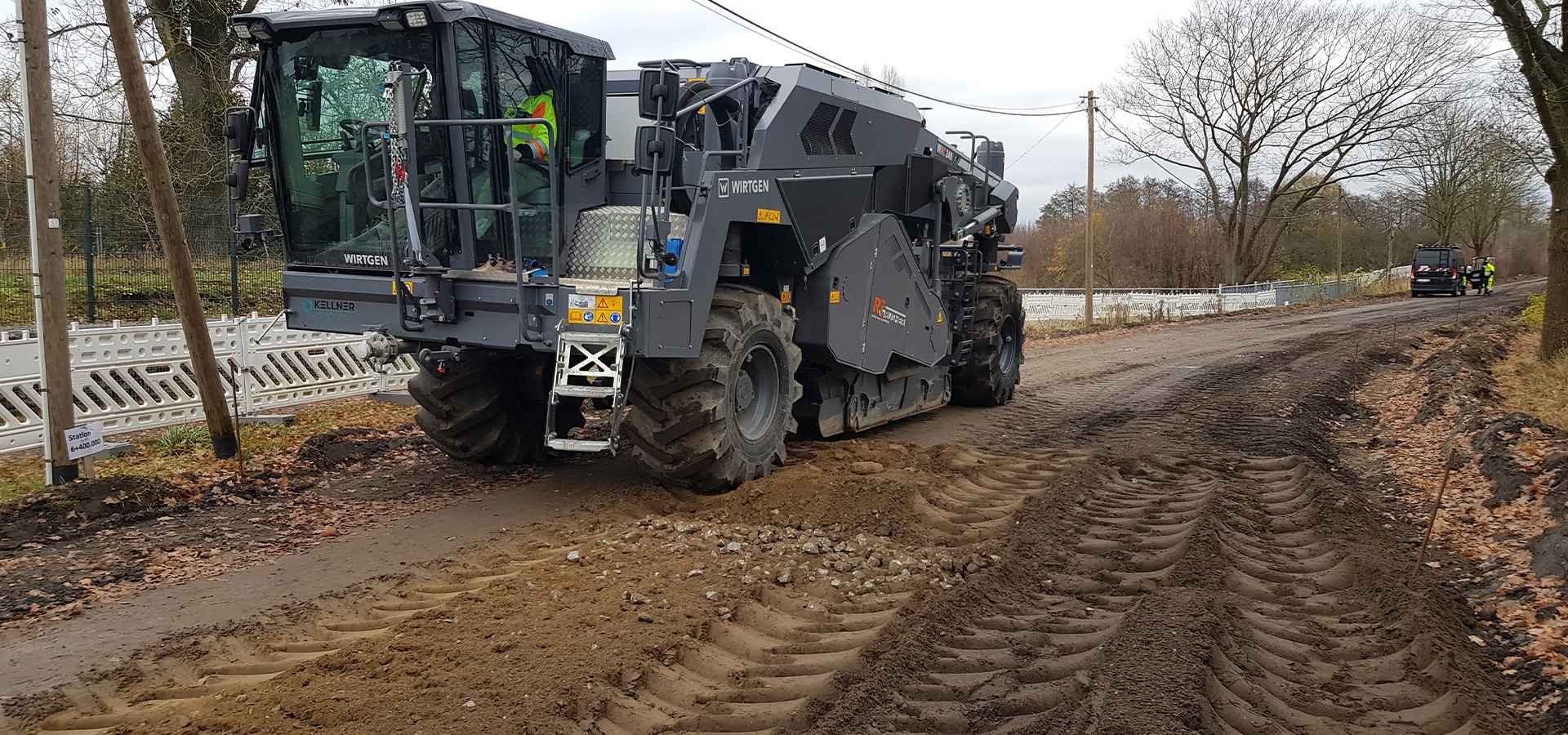 Graue Straßenfräse ohne sichtbaren Ausdruck auf brauner Baustelle mit tiefen Spuren