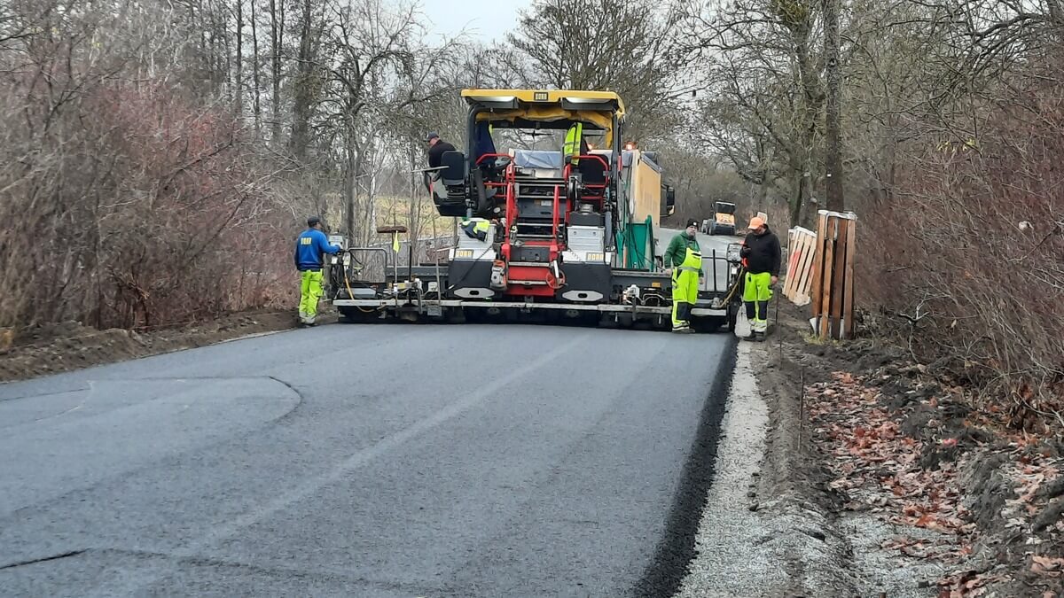 Straßenbauarbeiter in Neongelb arbeiten konzentriert an schwarzem Asphaltfertiger mit gelbem Dach