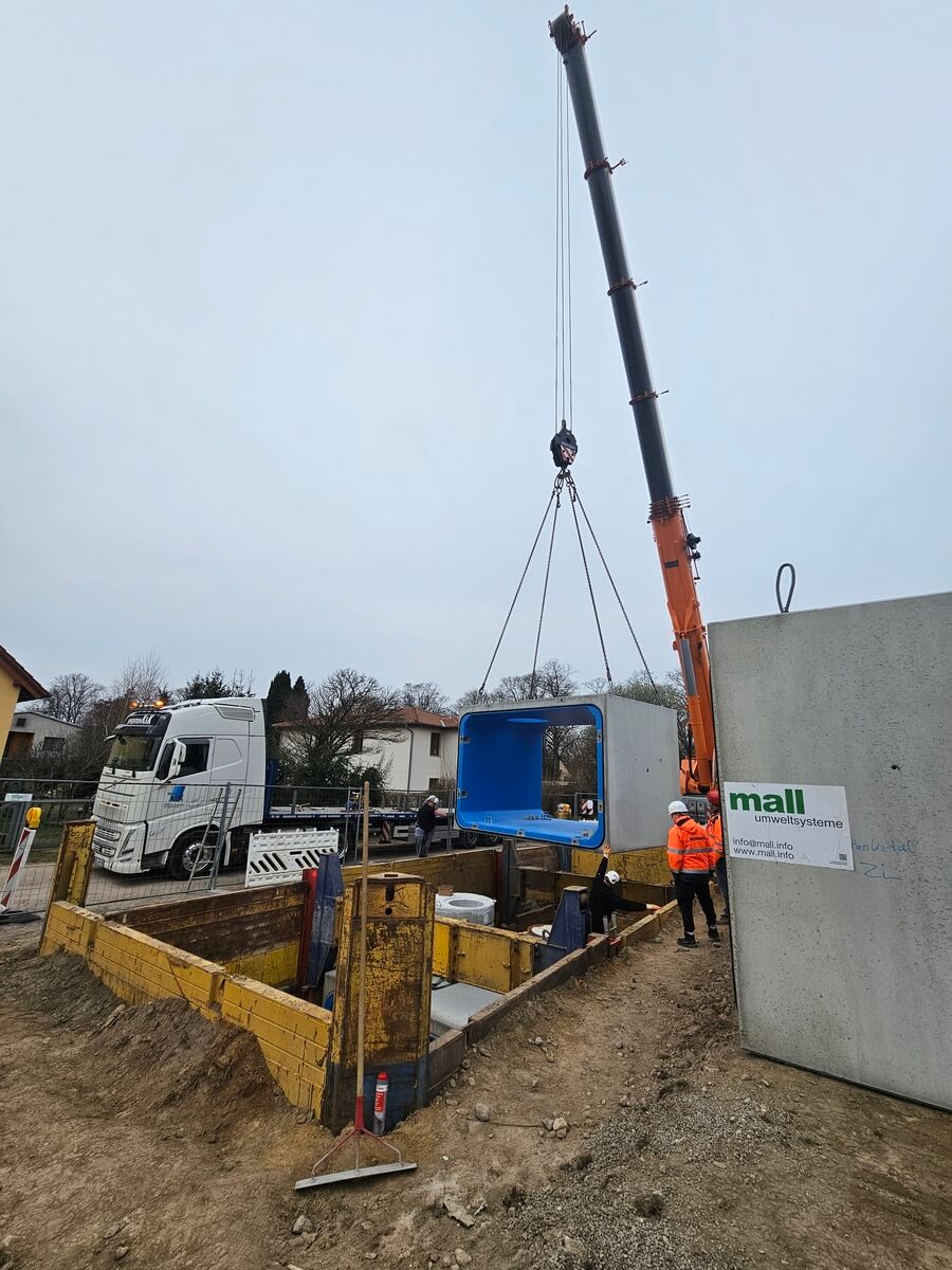 Bauarbeiter mit neutralem Blick heben blauen Tank per Kran in Grube