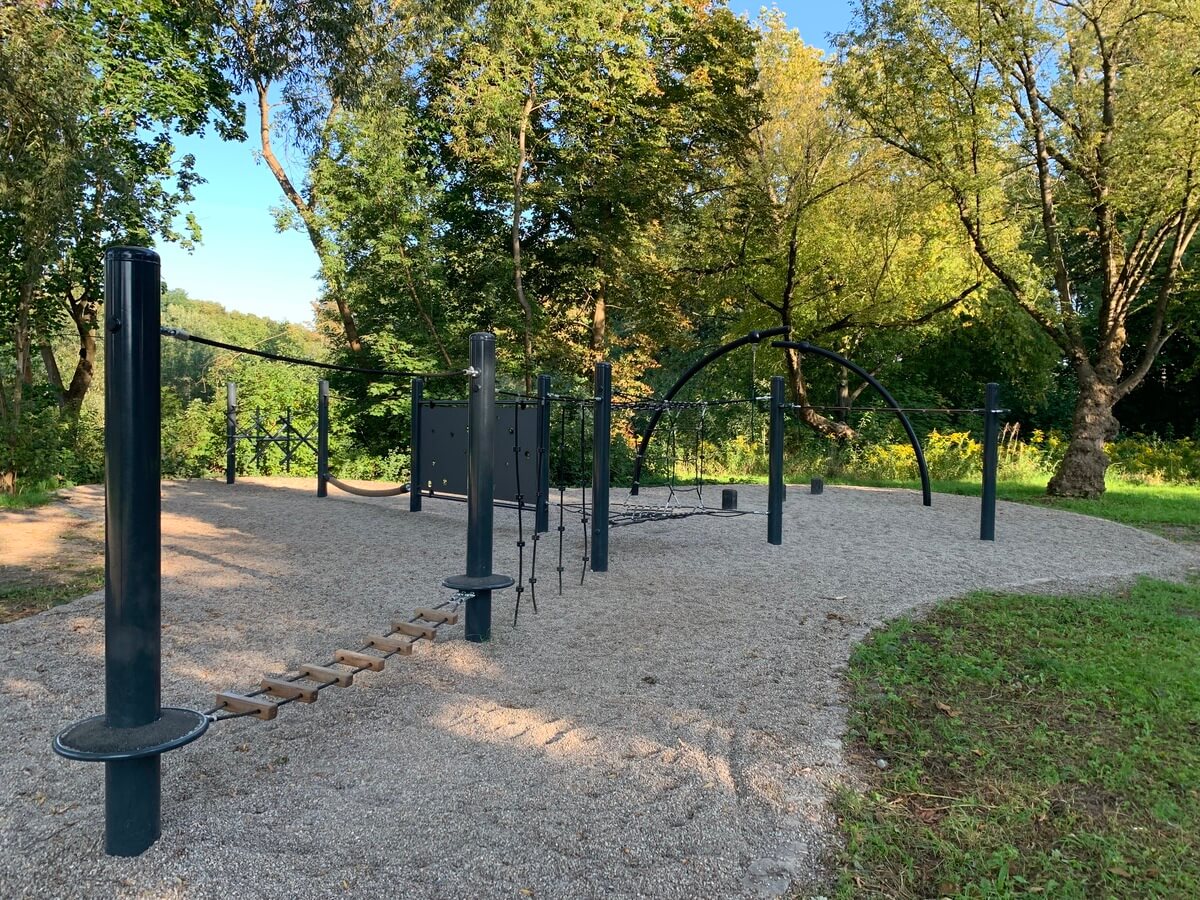 Leerer Kletterspielplatz in Gruen mit schwarzen Geraeten und Seilbruecke