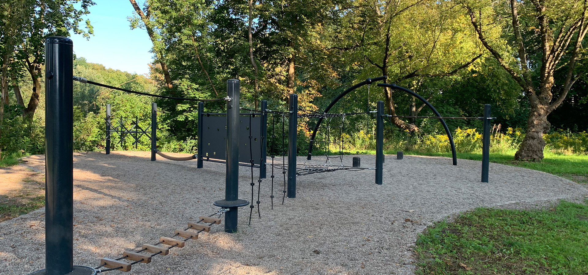 Leerer Outdoor Spielplatz mit schwarzen Kletterstangen auf Kies im Wald bei Sonne