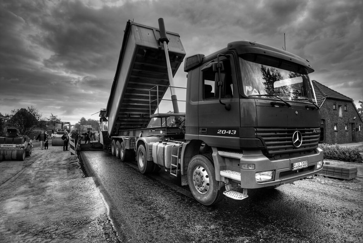 Schwarzer Kipper Lkw mit gehobener Mulde vor Wolkenhimmel und Baustelle