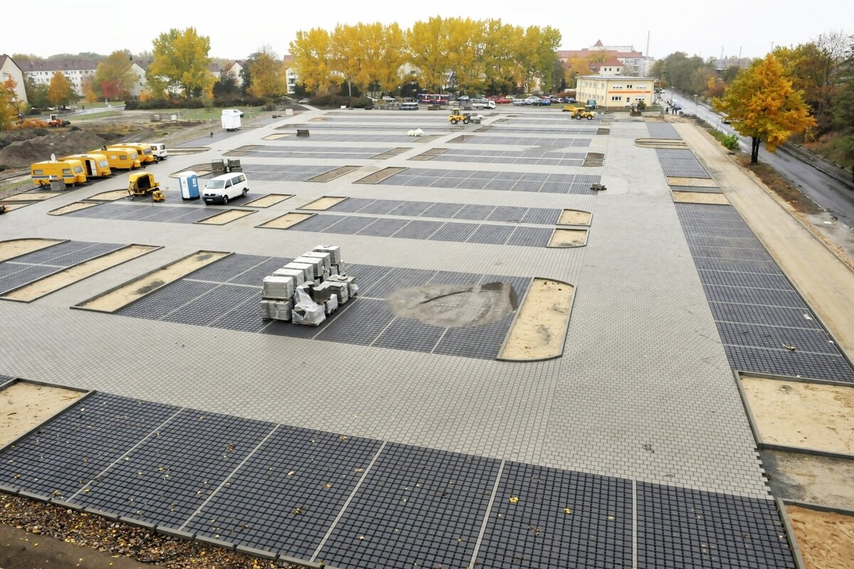 Weitlaeufiger grauer Platz mit schwarzen Matten und Fahrzeugen bei Herbstbaeumen
