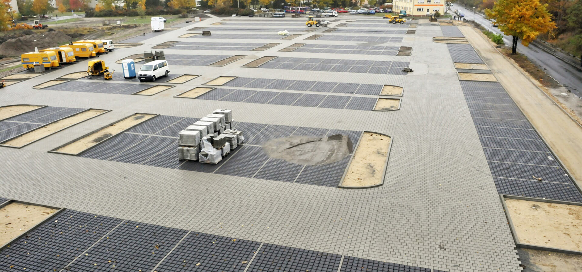 Luftbild von grauem Rasterplatz mit Fahrzeugen und Betonbloecken, herbstlich