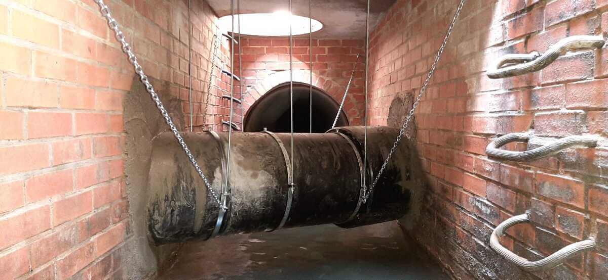 Grosse rostige Rohrsektion in Ziegelkanal mit Ketten und Lampenlicht