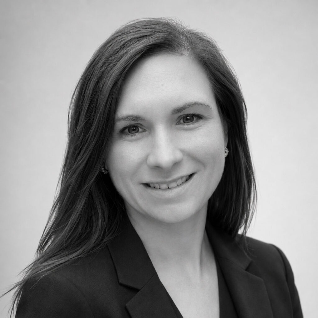 Frau mit neutralem Ausdruck, dunklem Haar, schwarzem Blazer, Portraet in Grau