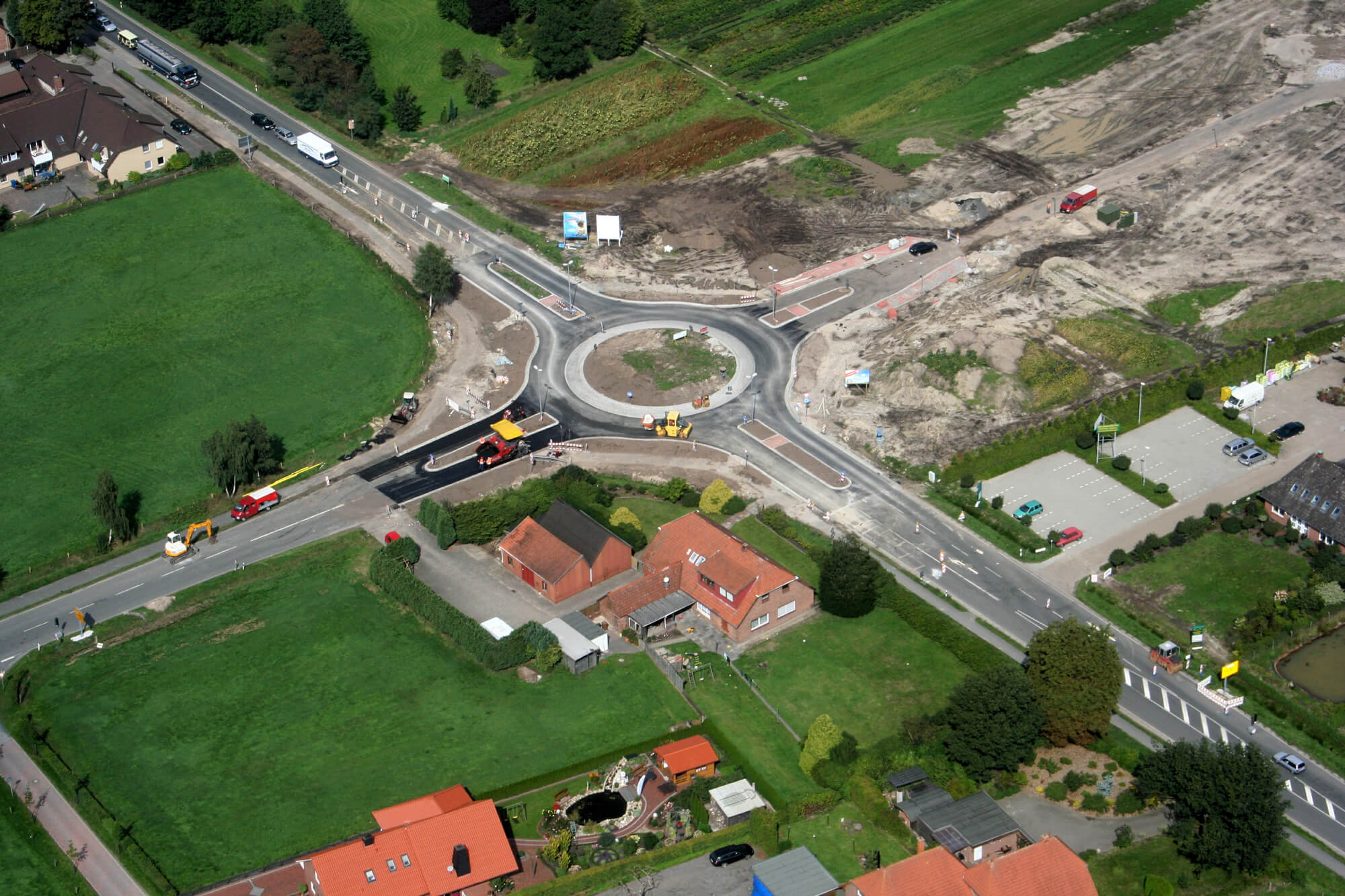 Luftbild eines Kreisverkehrs mit Baustelle, grauen Straßen und grünen Feldern
