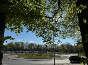 Kreisverkehr mit Pferdeskulptur unter gruenen Baeumen bei blauem Himmel