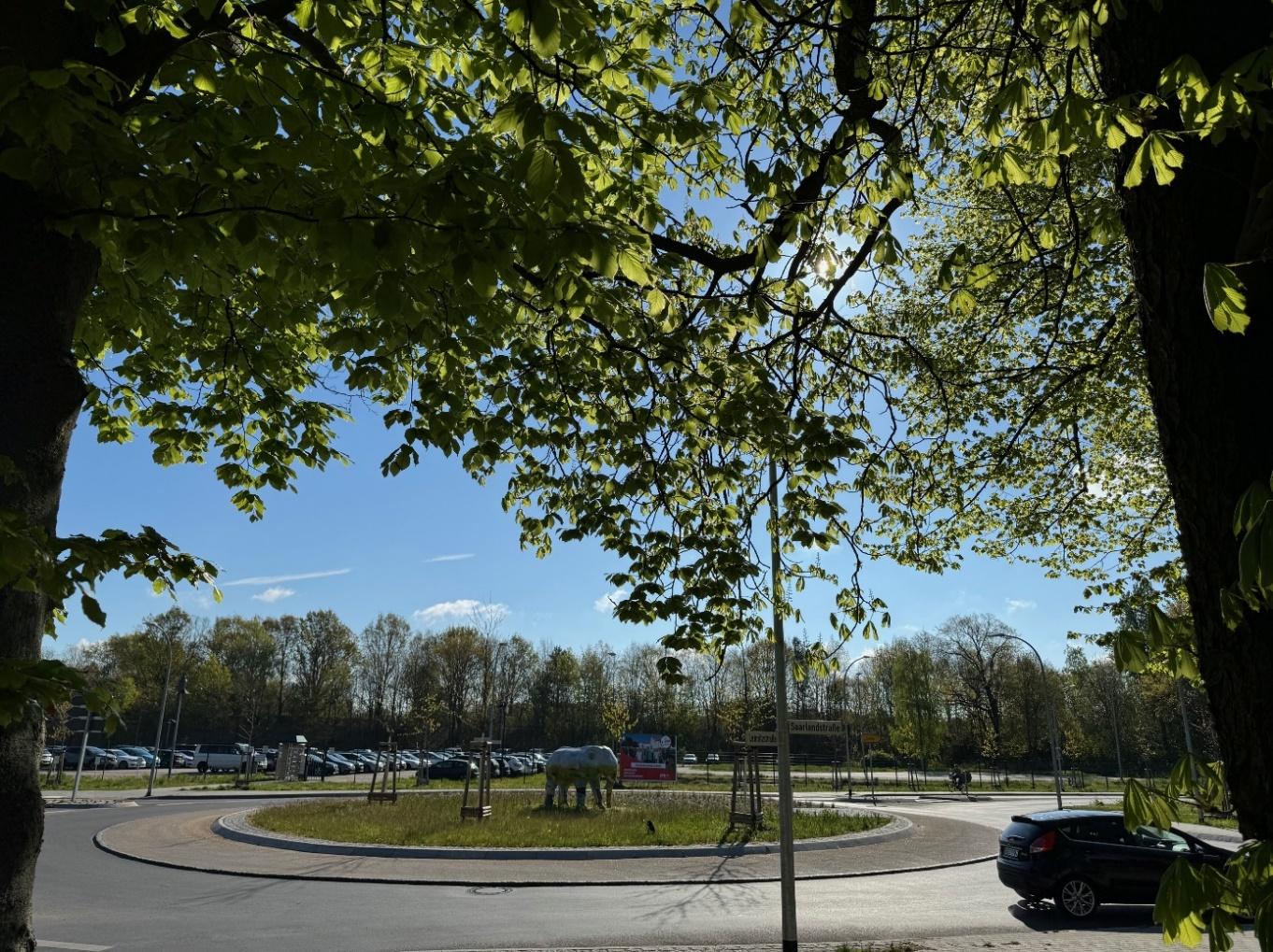 Kreisverkehr mit Pferdeskulptur unter gruenen Baeumen bei blauem Himmel